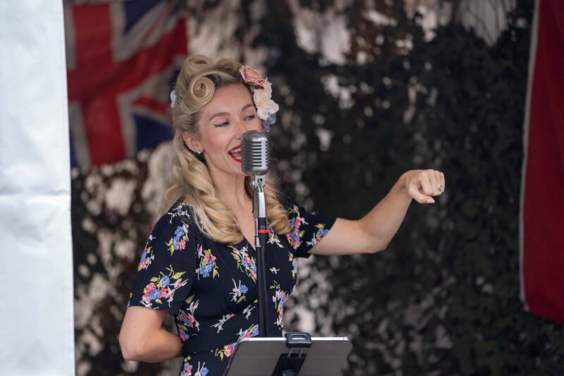 female singer in 1940s dress with 1940s hair style singing into a vintage microphone 