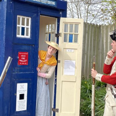 costumed lady leaning out of police box with soldier