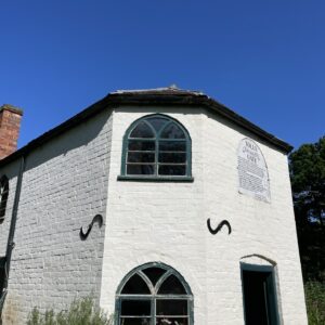 white Victorian toll house building with two arch windows and front door with blue sky