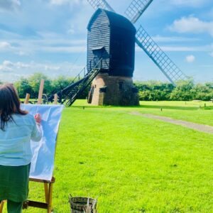 artist drawing on an easel with a field with windmill with blue sky