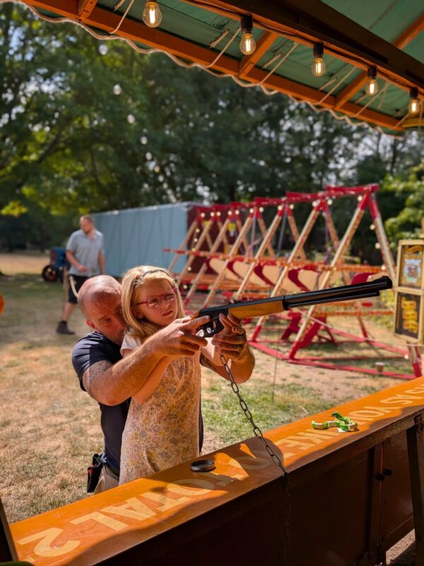 child with a man firing at the fairground riffle range 